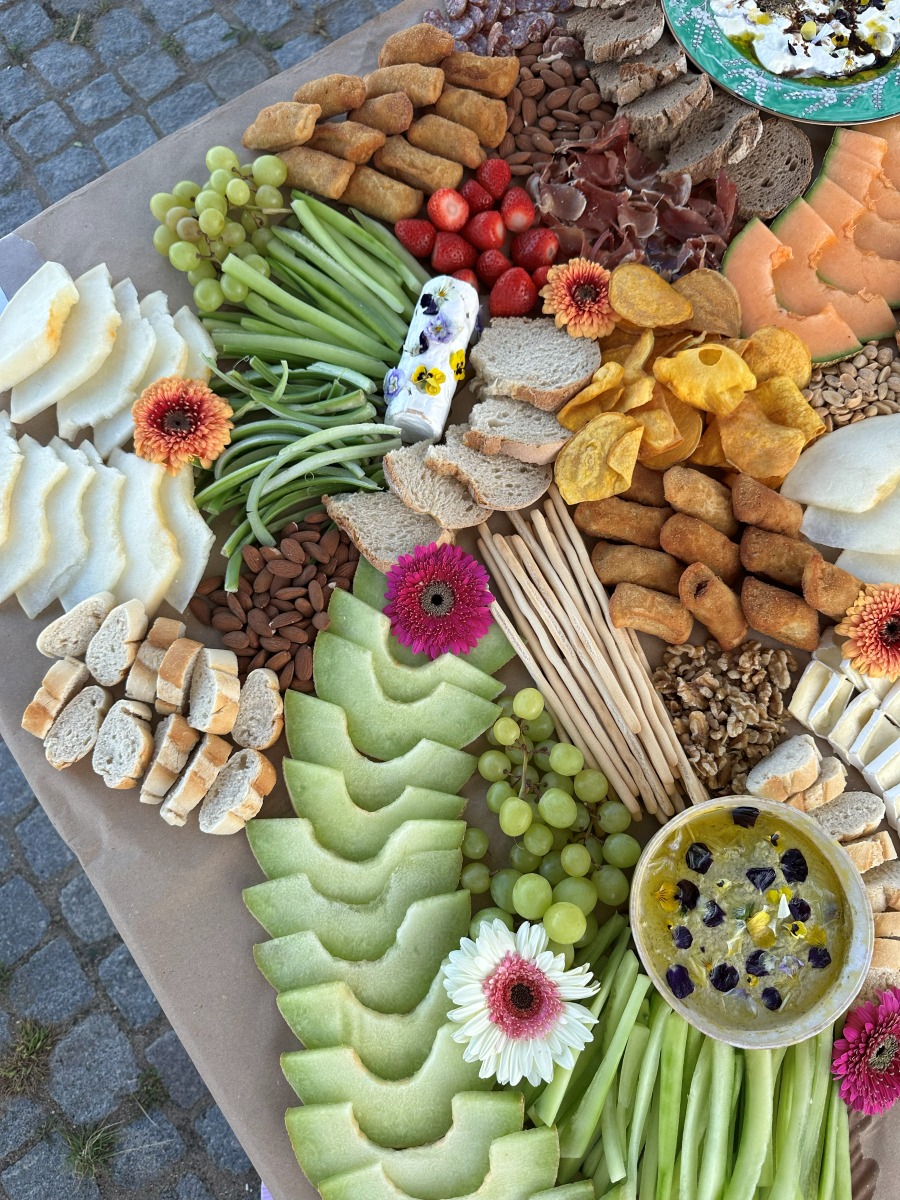 Overhead view of an abundant grazing table with breadsticks, dips, melon and fresh flowers