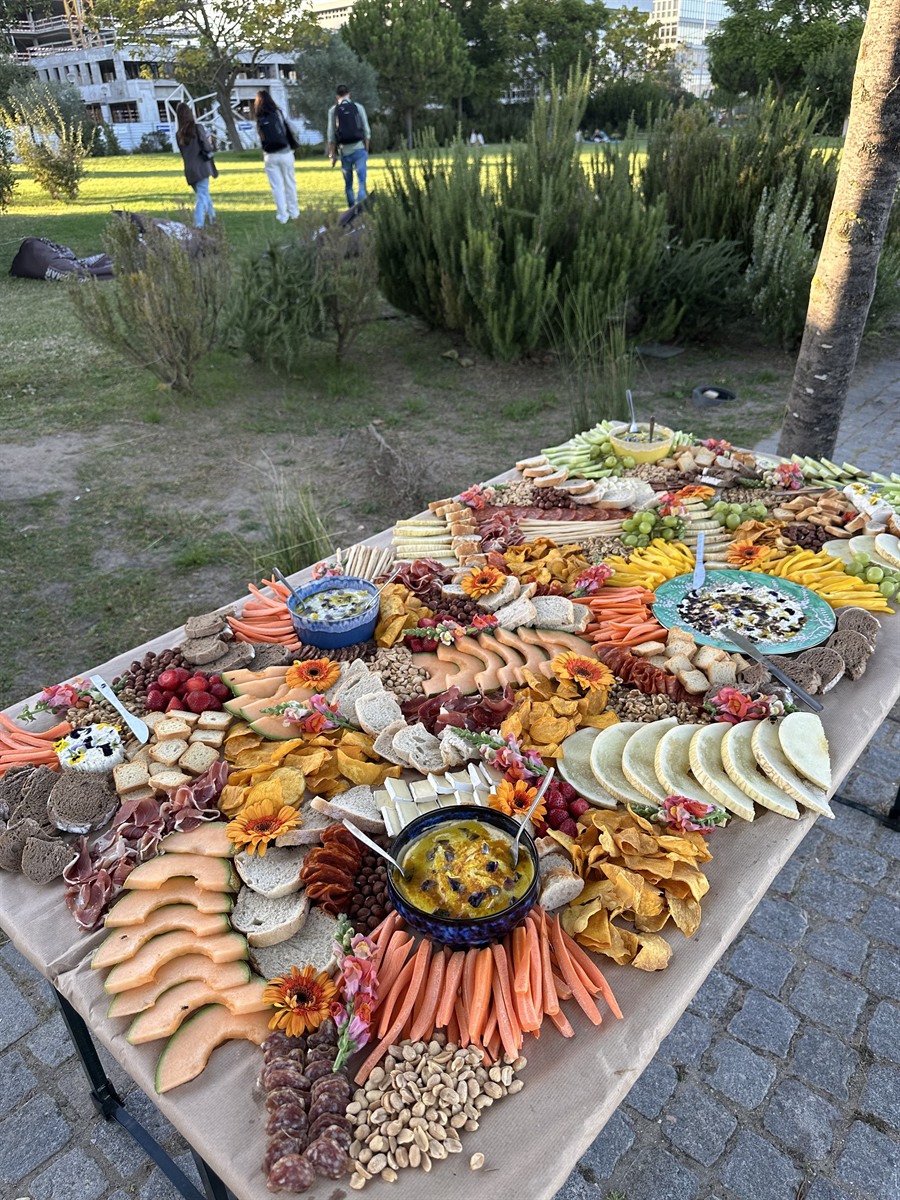 A long outdoor grazing table set in a park at golden hour, styled with dips, meats and flowers