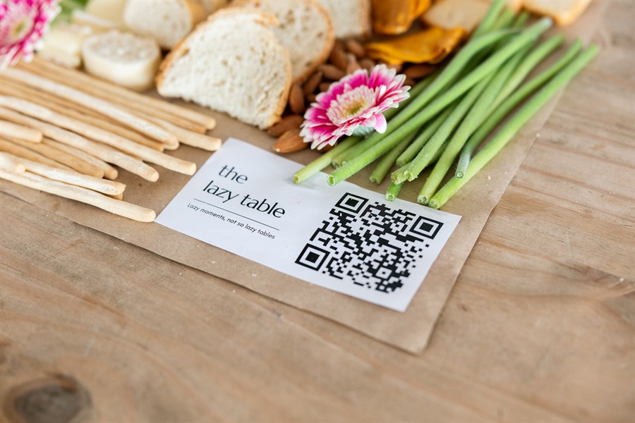 The Lazy Table card beside breadsticks, bread and fresh flowers
