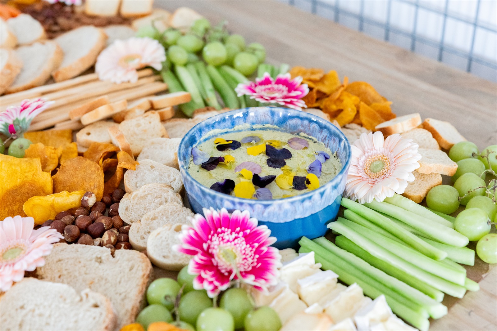 An abundant grazing table with breads, crudites, grapes, edible flowers and a dip bowl