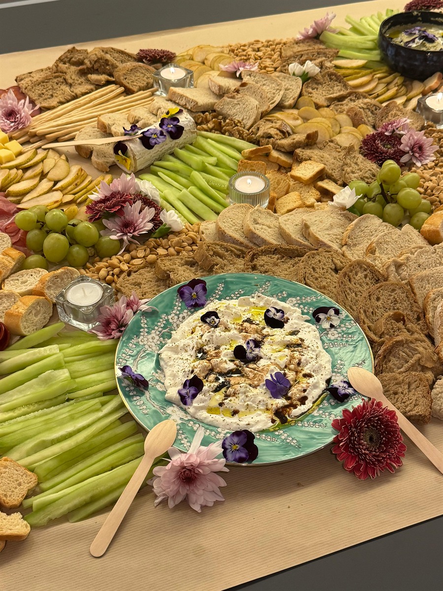 A long grazing table with dips on a painted plate, crudités, breads and edible flowers