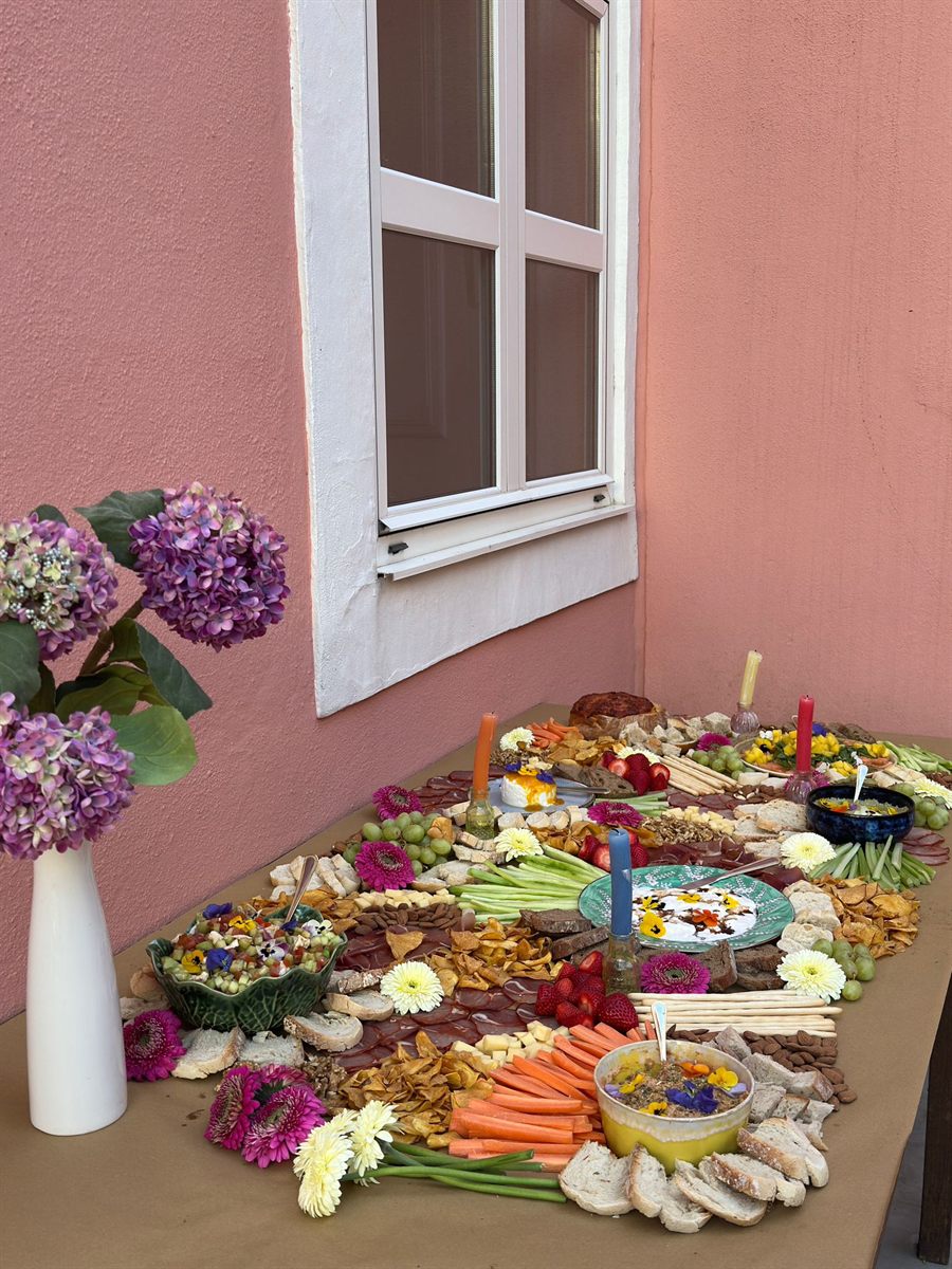 A colourful grazing table styled with fresh flowers against a pink wall
