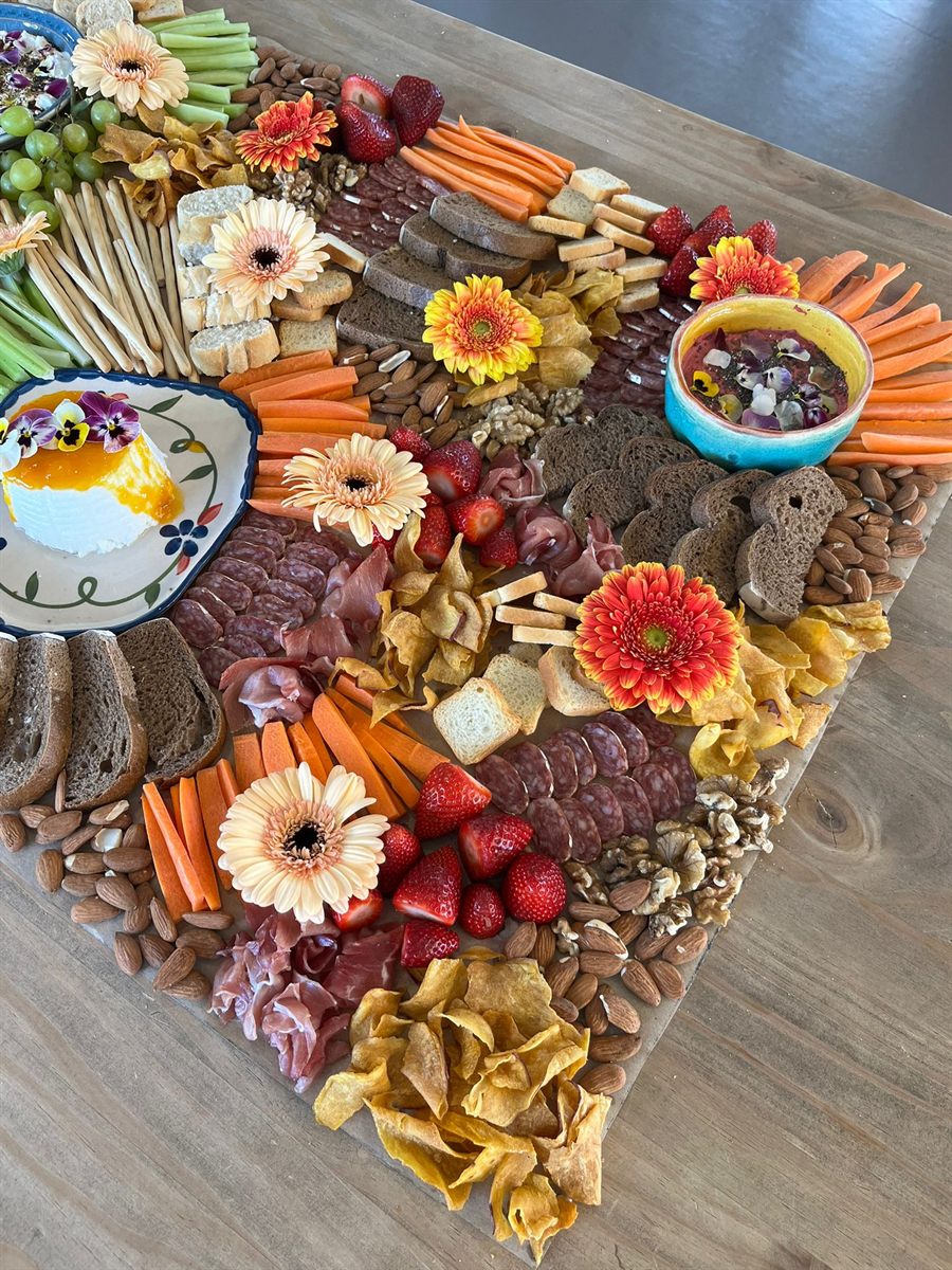 A grazing board with charcuterie, cheese, fruit and edible flowers